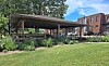 Covered outdoor seating area in a courtyard with people seated, green grass, and brick buildings in the background.