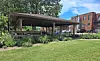 Covered outdoor seating area in a courtyard with people seated, green grass, and brick buildings in the background.