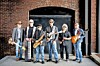 Five men holding instruments pose in front of a brick archway and doorway.