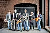 Five men holding instruments pose in front of a brick archway and doorway.