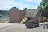 A damaged house with a collapsed porch roof and a black SUV parked in front.