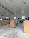 Cardboard boxes stacked on blue pallets inside a warehouse with concrete floors and exposed ceiling fixtures.