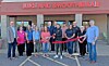 People stand in a line outside Juice and Smoothie Bar holding a red ribbon at a ribbon-cutting event.