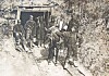 Workers stand with a mule-drawn cart at a tunnel entrance carved into a rocky hillside.