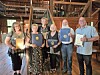 Five people stand together indoors holding framed awards in front of bookshelves and a wooden staircase.