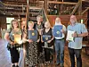 Five people stand together indoors holding framed awards in front of bookshelves and a wooden staircase.