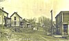 Historic residential street with dirt road, wooden houses, and utility poles under a bare winter sky.