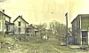 Historic residential street with dirt road, wooden houses, and utility poles under a bare winter sky.
