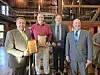 Four men pose indoors holding award plaques and a medallion in a wooden room.