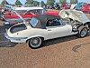 White vintage convertible parked next to a crumpled trailer in an outdoor car lot.