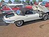 White vintage convertible parked next to a crumpled trailer in an outdoor car lot.