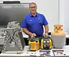 Man in a blue polo stands behind portable generators and power equipment displayed on a table.