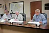 Three officials seated at a conference table reviewing documents in a meeting room.