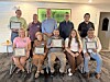 A group of people pose indoors, many holding framed certificates and plaques.