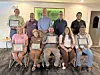 A group of people pose indoors, many holding framed certificates and plaques.