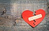 Broken red paper heart with a bandage on a wooden wood-grain surface.