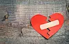 Broken red paper heart with a bandage on a wooden wood-grain surface.