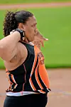 An athlete in orange and black prepares to throw on an outdoor track and field area.