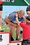Athlete bends forward while a presenter puts a medal around her neck on a podium.