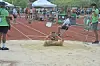 Athlete landing in a sand pit during a long jump at an outdoor track and field event.