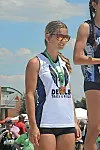 Athlete wearing sunglasses and a medal stands on a podium at an outdoor track and field event.