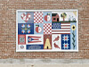 Colorful quilt-style mural with geometric shapes and birds on a brick wall.