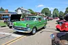 A green vintage car parked on a street surrounded by other classic cars at an outdoor show.