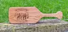Wooden paddle with an engraved design lying on a weathered log in front of grass.