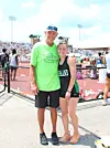 Two athletes pose together near a track and field stadium with spectators behind them.