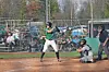 Batter waiting at home plate with catcher crouched behind and umpire standing nearby on a baseball field.