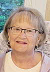 Portrait of an older woman wearing glasses and hoop earrings indoors.