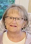 Portrait of an older woman wearing glasses and hoop earrings indoors.