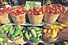 Woven baskets filled with tomatoes, cucumbers, and yellow squash at a produce stand.