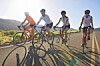Four cyclists riding on a road under bright sunlight.