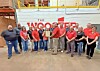 Group of employees posing in a warehouse in front of a large sign that reads The Woodfibre.