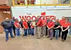 Group of employees posing in a warehouse in front of a large sign that reads The Woodfibre.