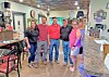 Five people standing inside a restaurant with tables, chairs, and a counter area.