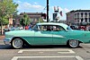 Mint-green vintage car parked on a city street with buildings and traffic lights behind it.