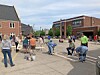 People gathered on a street near brick buildings and sidewalks under a partly cloudy sky.