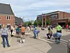 People gathered on a street near brick buildings and sidewalks under a partly cloudy sky.