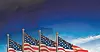 Several American flags on poles waving in the wind against a blue sky.