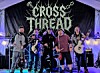 A band performs onstage under a tent with guitars, drums, and stage lighting.