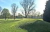 A grassy mound in a park with bare trees and open green lawn under a clear sky.