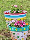 Colorful painted planter with blooming flowers arranged in tiers on a grassy lawn.