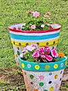 Colorful painted planter with blooming flowers arranged in tiers on a grassy lawn.