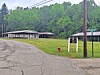 Paved road beside a grassy area with shelters, utility poles, and trees on a hillside.