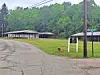 Paved road beside a grassy area with shelters, utility poles, and trees on a hillside.