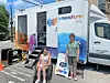 Momentum mobile clinic parked outside with two people nearby and a wheelchair at the entrance.