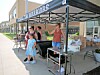 People stand under a canopy tent beside a table with supplies outside a storefront.