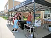 People stand under a canopy tent beside a table with supplies outside a storefront.
